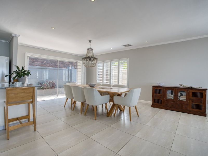 Spacious open-plan dining and kitchen area featuring neutral tiled flooring, recessed lighting, and large sliding doors with plantation shutters leading to the exterior.