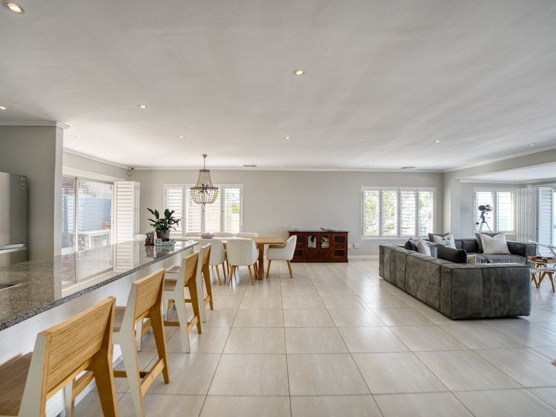 Spacious open-plan living area featuring a modern kitchen with granite countertops, tiled flooring, and large windows with plantation shutters offering natural light.