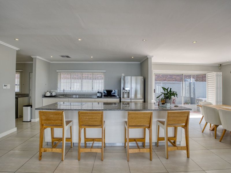 Spacious open-plan kitchen and dining area featuring a large granite-topped island, modern cabinetry, recessed lighting, and seamless access to the outdoor patio.