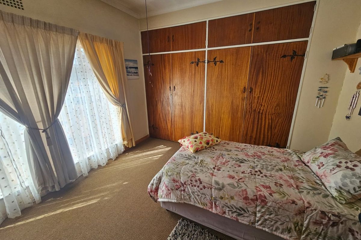 A bedroom featuring built-in wooden wardrobes and carpeted flooring, offering a functional space with natural light.