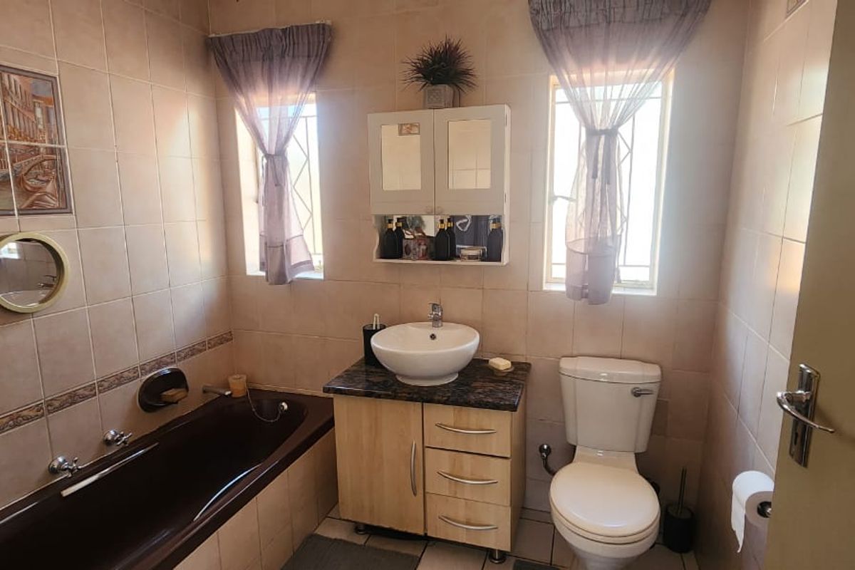 A functional bathroom featuring a built-in bathtub, vanity cabinet with vessel sink, and a standard toilet, finished with full-height wall tiling.