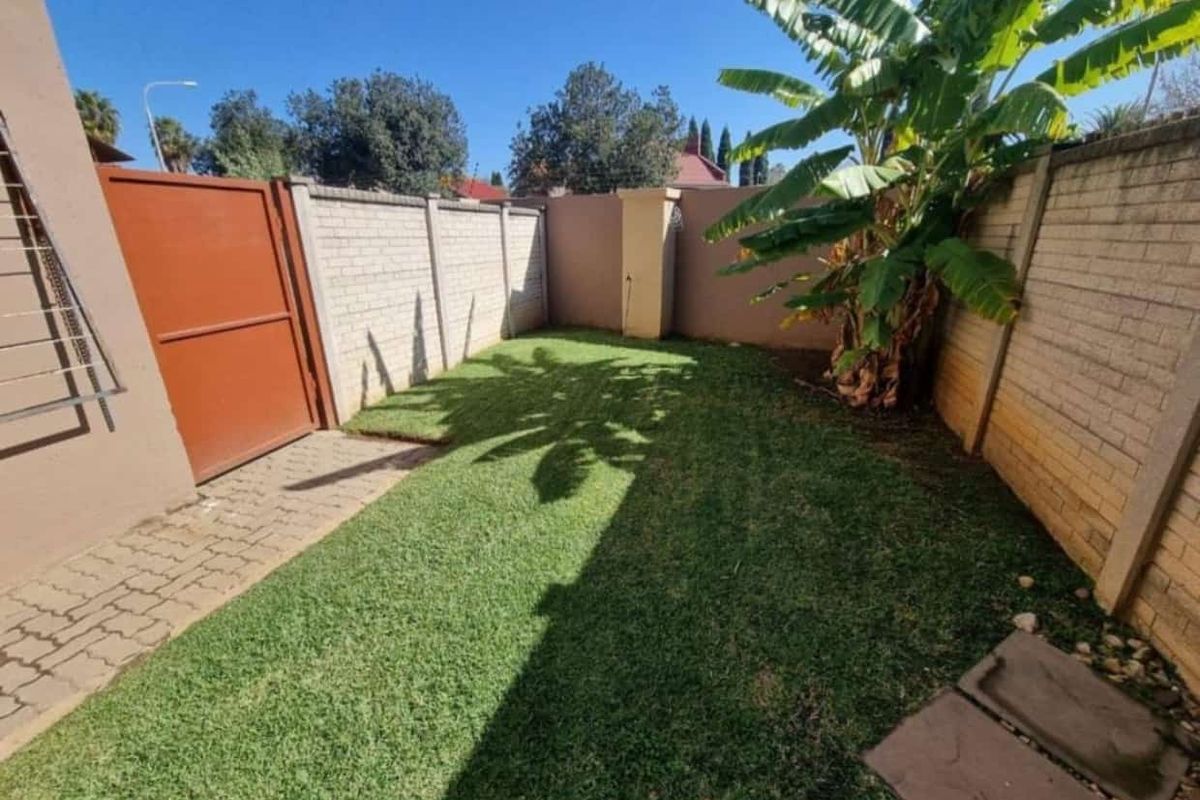 A private rear garden area featuring a lawn, paved walkway, and secure perimeter boundary walls with a metal access gate.