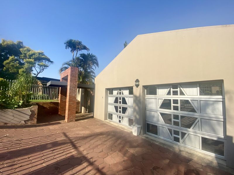 A double garage with decorative panel doors, paved driveway, and a brick entrance feature, set against a clear blue sky.