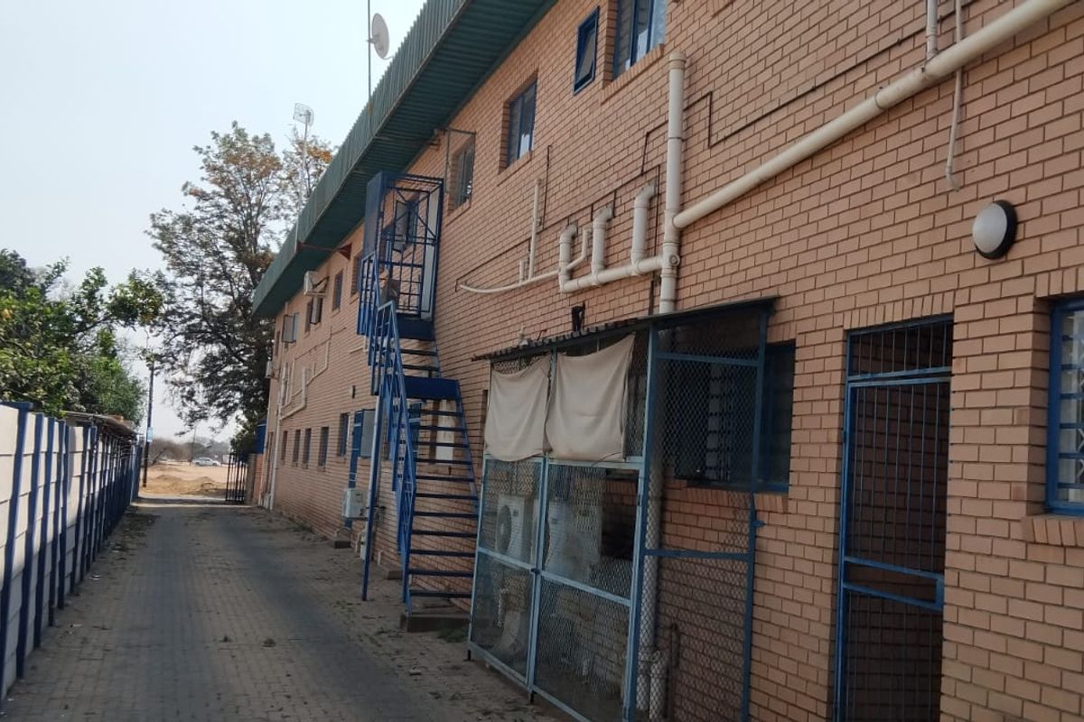 Side exterior view of a commercial brick building featuring a metal external staircase, security fencing, and paved walkway access.