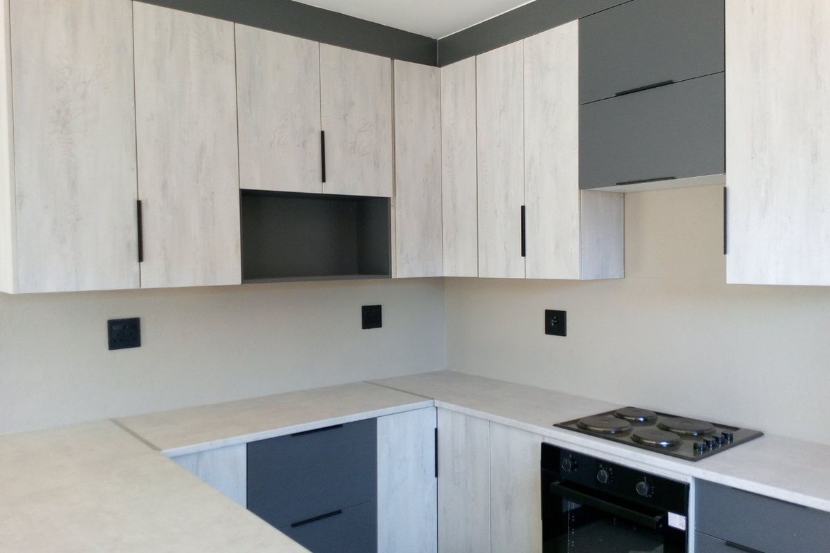 Modern kitchen featuring two-tone cabinetry, integrated electric oven, and built-in hob with light-toned countertops.