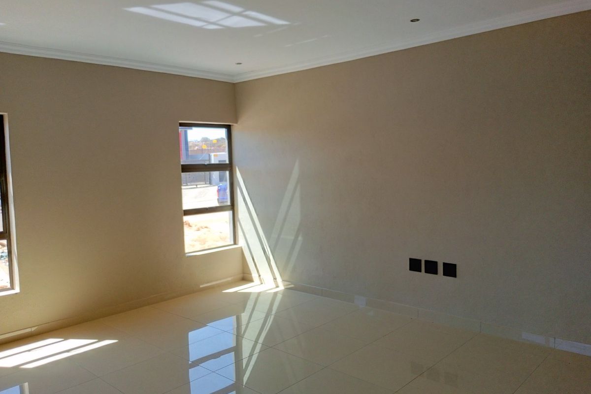 A bright, empty living room featuring polished porcelain floor tiles, neutral wall finishes, and modern recessed ceiling lighting.