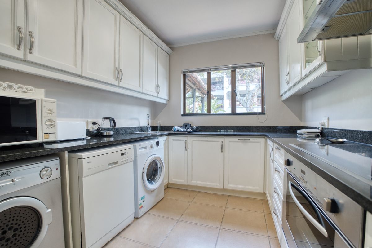 A functional kitchen featuring white cabinetry, dark granite countertops, tiled flooring, and integrated appliances including an oven and extractor fan.
