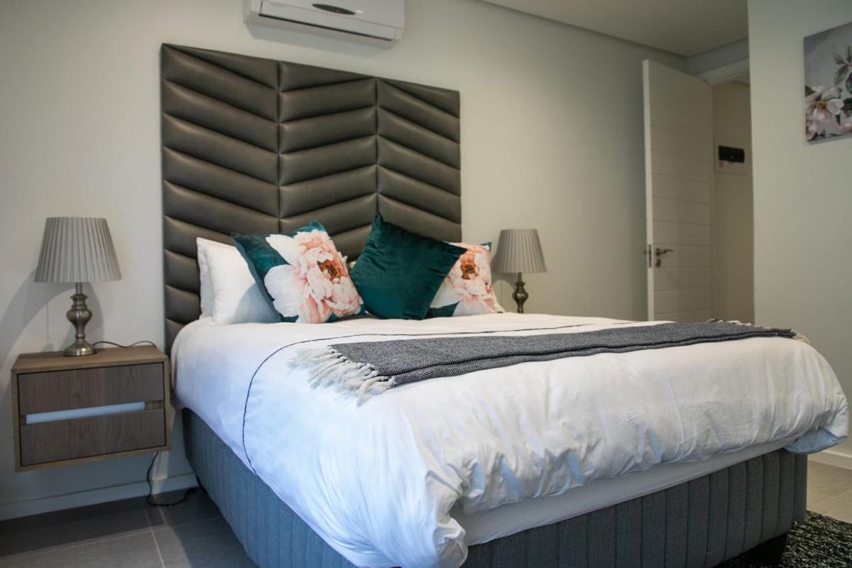 A well-maintained bedroom featuring a modern upholstered headboard, wall-mounted air conditioning unit, and neutral tiled flooring.