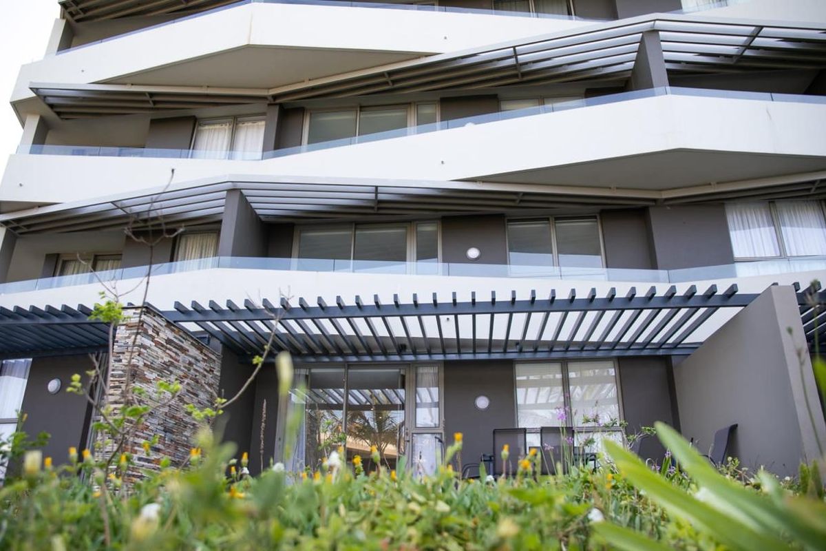 A low-angle view of a modern apartment building facade featuring tiered balconies with glass railings and dark metal pergola structures.