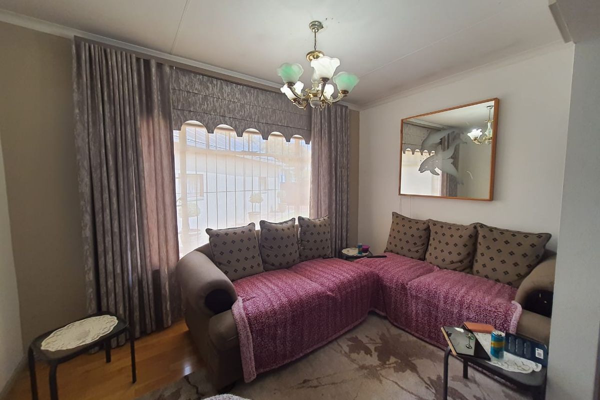 A cozy living room featuring hardwood flooring, a large window with decorative curtains, and a central chandelier.