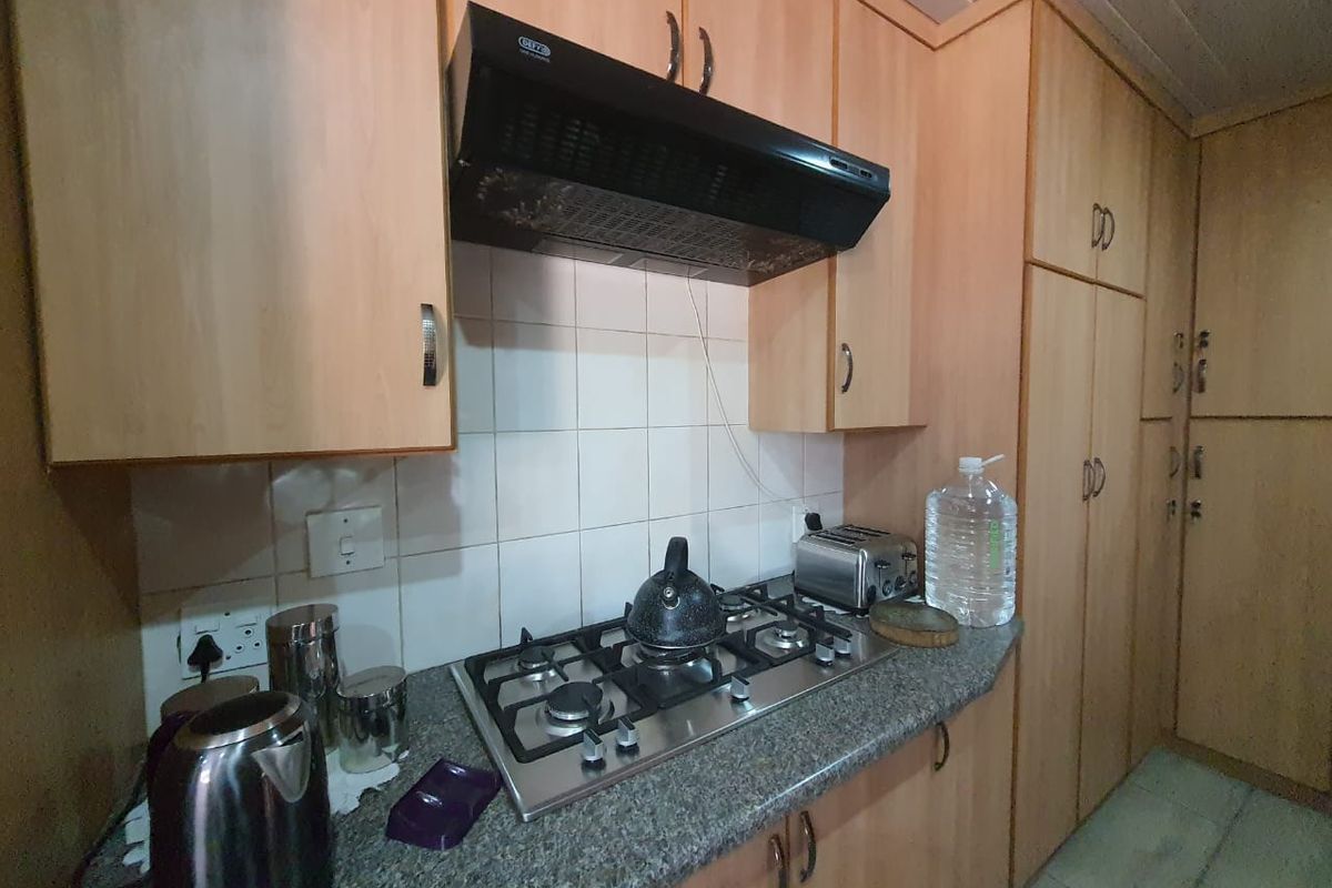 A functional kitchen featuring light wood-finish cabinetry, a granite-look countertop, a gas hob, and a black extractor fan.