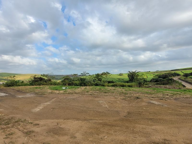 Expansive rural landscape view featuring rolling hills, agricultural fields, and a dirt access track under a cloudy sky.