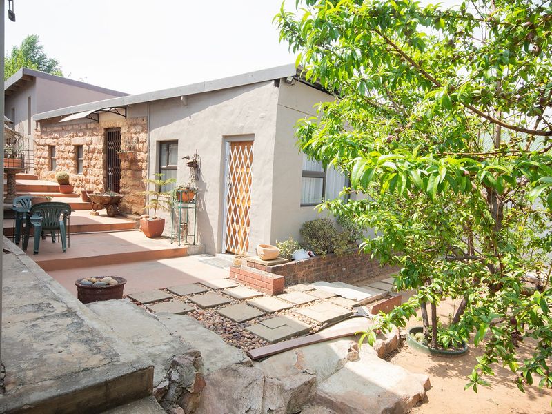 Rear exterior view featuring a stone masonry wall, concrete patio area, and stepped terrace leading to the building entrance.