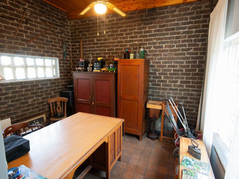 A utility room featuring exposed brick walls, terracotta floor tiles, and a timber ceiling, currently utilized as a workspace or storage area.