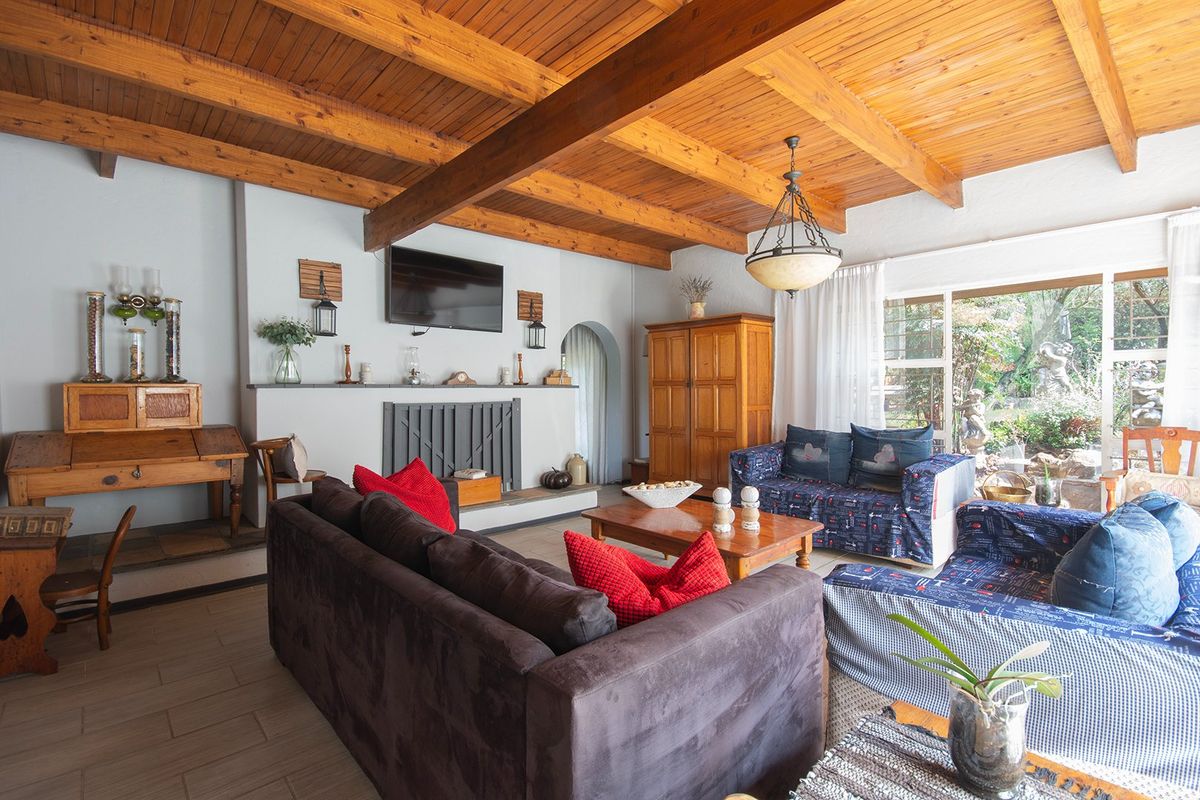 Spacious living room featuring exposed timber ceiling beams, a central fireplace, and large sliding glass doors providing natural light and garden access.