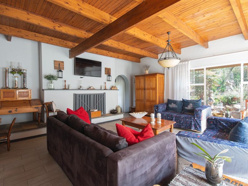 Spacious living room featuring exposed timber ceiling beams, a central fireplace, and large sliding glass doors providing natural light and garden access.