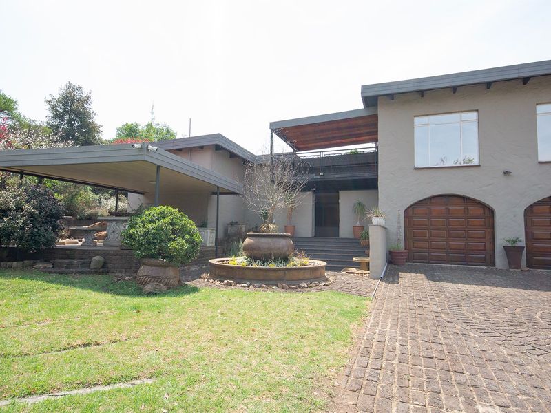 Front elevation of a multi-level home featuring a paved driveway, double garage, covered patio area, and a central garden water feature.