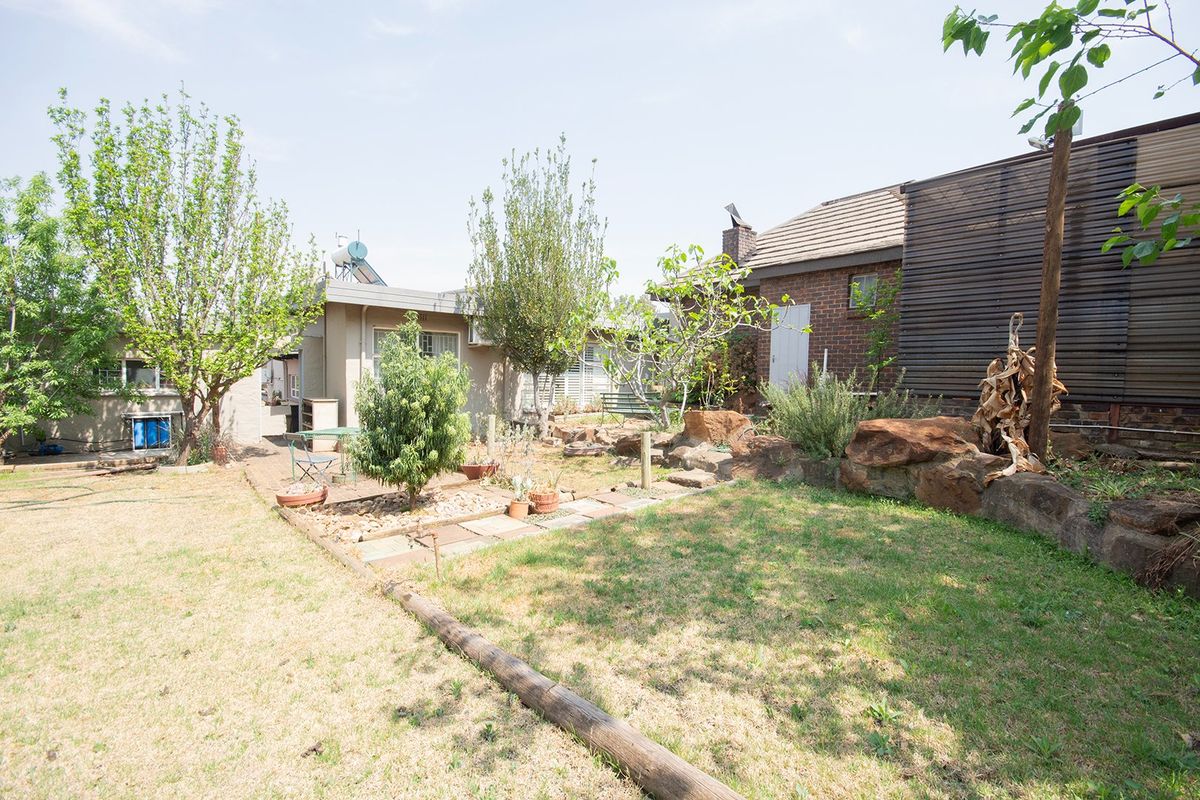 A rear garden area featuring a stone retaining wall, paved pathways, and a brick exterior facade with a solar water heating system.