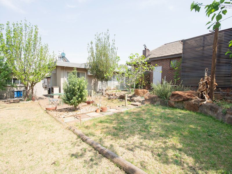A rear garden area featuring a stone retaining wall, paved pathways, and a brick exterior facade with a solar water heating system.