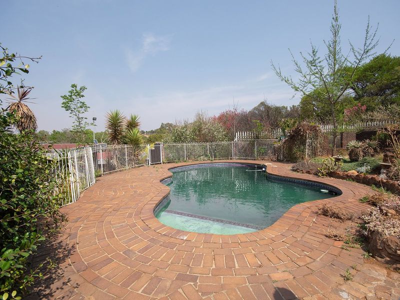 Outdoor pool area featuring a kidney-shaped swimming pool surrounded by brick paving and enclosed by metal perimeter fencing.