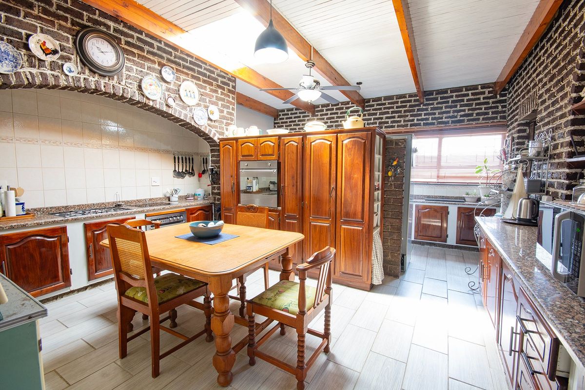 Spacious kitchen featuring exposed brick walls, timber ceiling beams, a skylight, granite countertops, and extensive built-in wooden cabinetry.