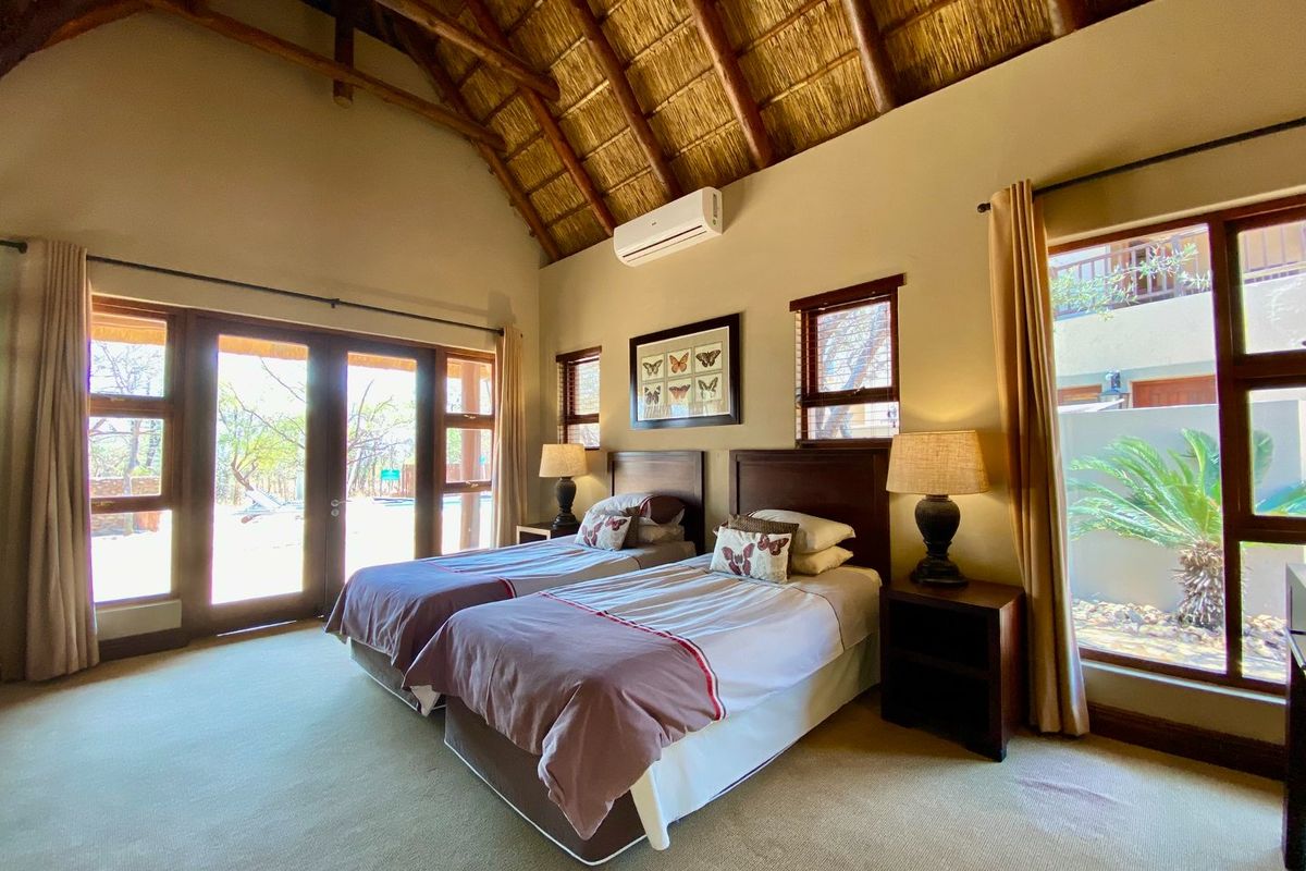 Spacious bedroom featuring a high vaulted thatched ceiling, split-system air conditioning, and large windows providing natural light and garden views.