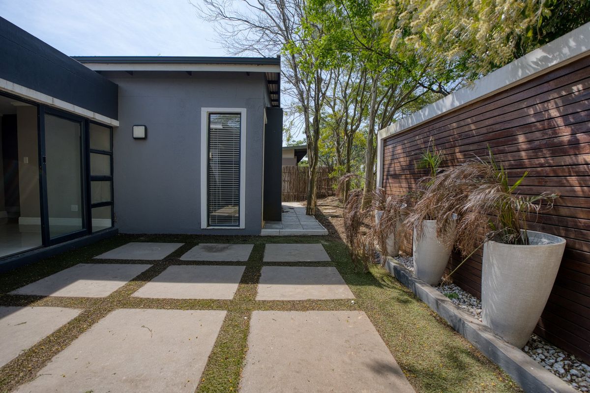 A modern rear exterior area featuring a paved patio, timber slat boundary fencing, and established trees, providing a private outdoor space.