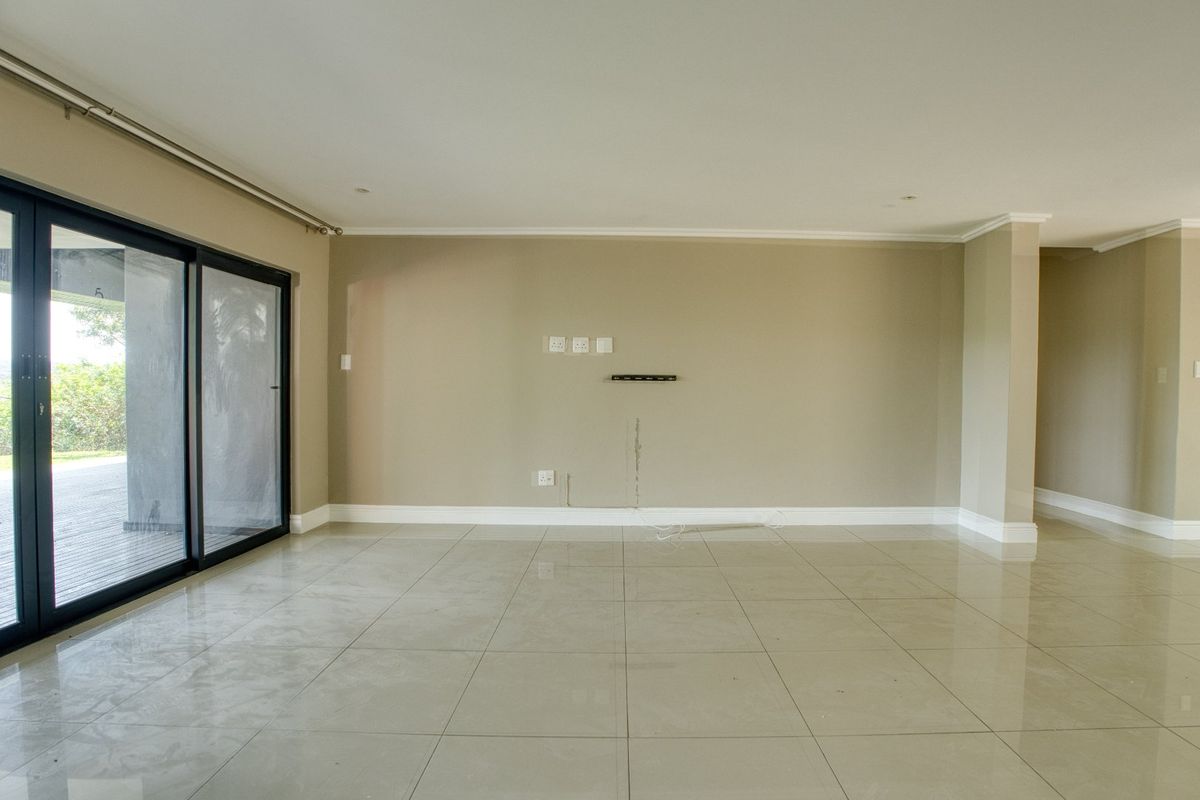 A spacious, empty living area featuring large sliding glass doors, neutral tiled flooring, and integrated wall-mounted electrical and media connection points.