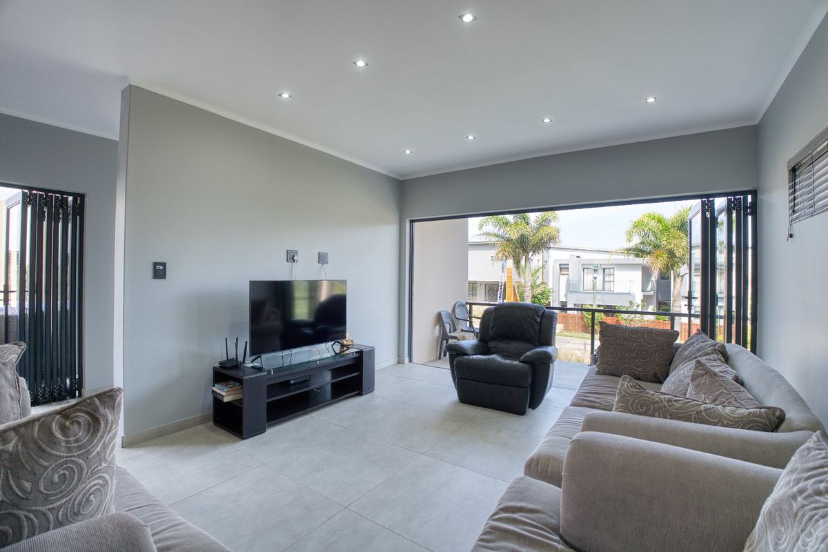 Modern living room featuring large format floor tiles, recessed downlighting, and wide folding doors opening onto a private balcony.