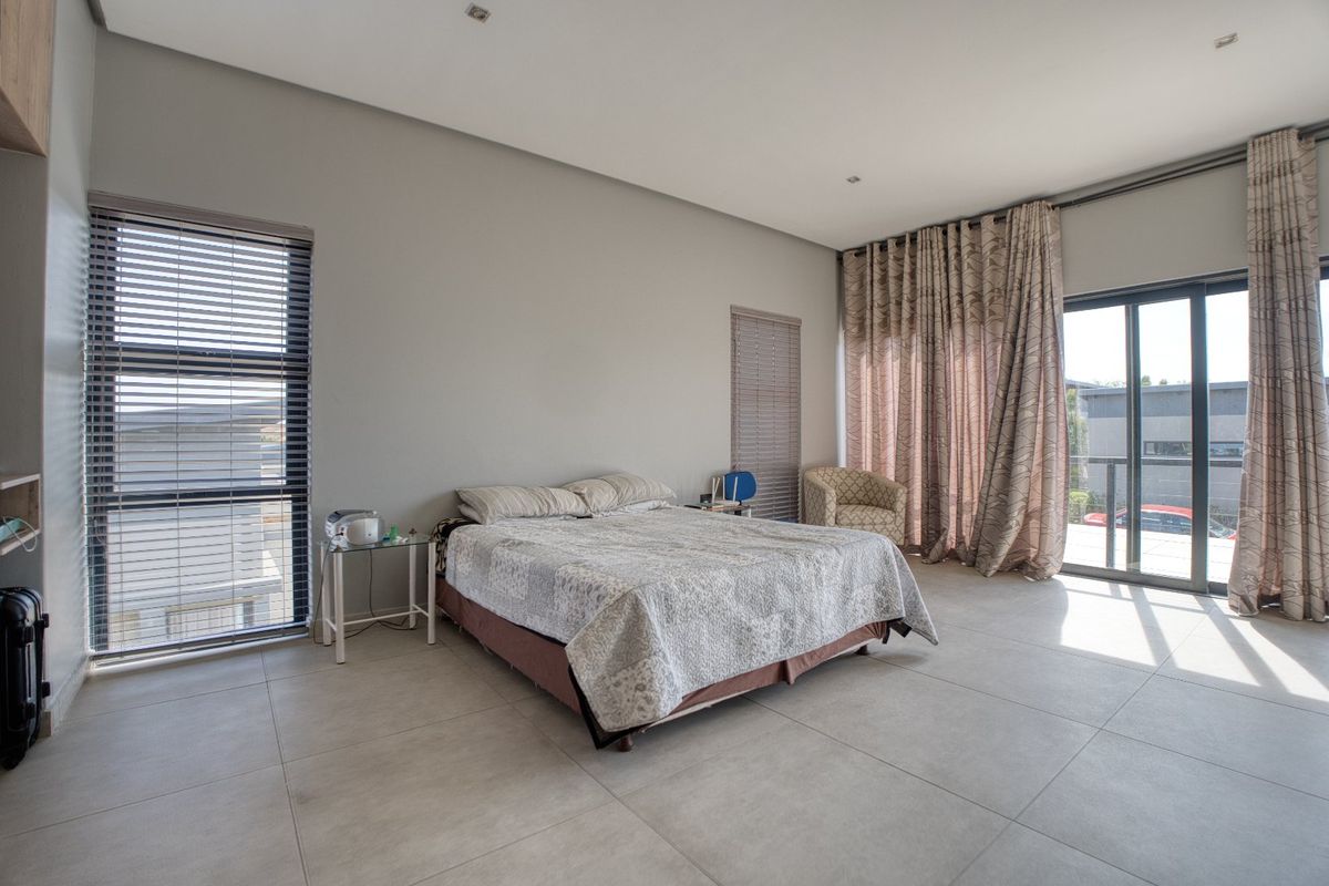 Spacious bedroom featuring large format floor tiles, recessed ceiling lighting, and sliding glass doors providing access to an outdoor balcony area.