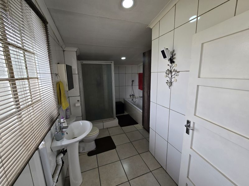 A functional bathroom featuring a pedestal basin, a separate shower enclosure, and a built-in bathtub with tiled finishes throughout.