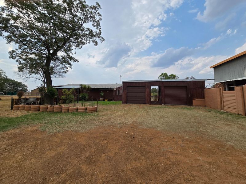 Exterior view of a farm property featuring a double garage with roller shutter doors, corrugated metal roofing, and surrounding perimeter fencing.