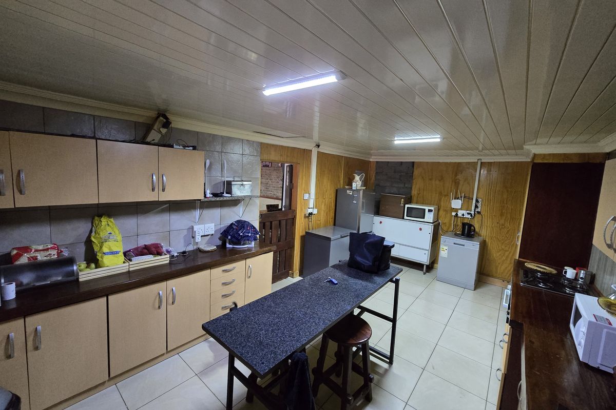 A functional kitchen featuring laminate cabinetry, tiled flooring, and a central island, with wood-panelled walls and practical tiled backsplash areas.
