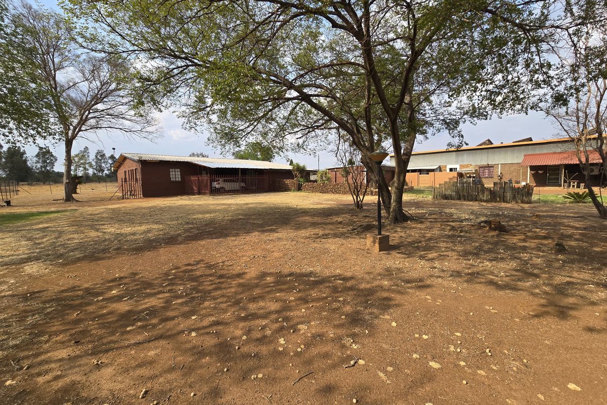 Spacious rear yard area featuring mature trees, open ground, and views of the farm outbuildings with corrugated metal roofing and timber siding.