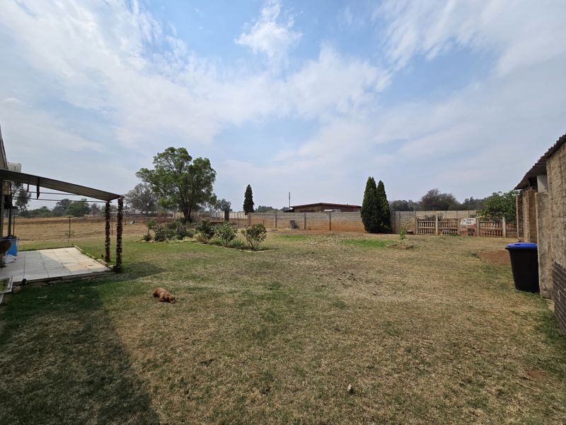 Spacious rear garden area featuring a covered tiled patio, expansive lawn, and perimeter walling, offering potential for outdoor landscaping and entertainment development.