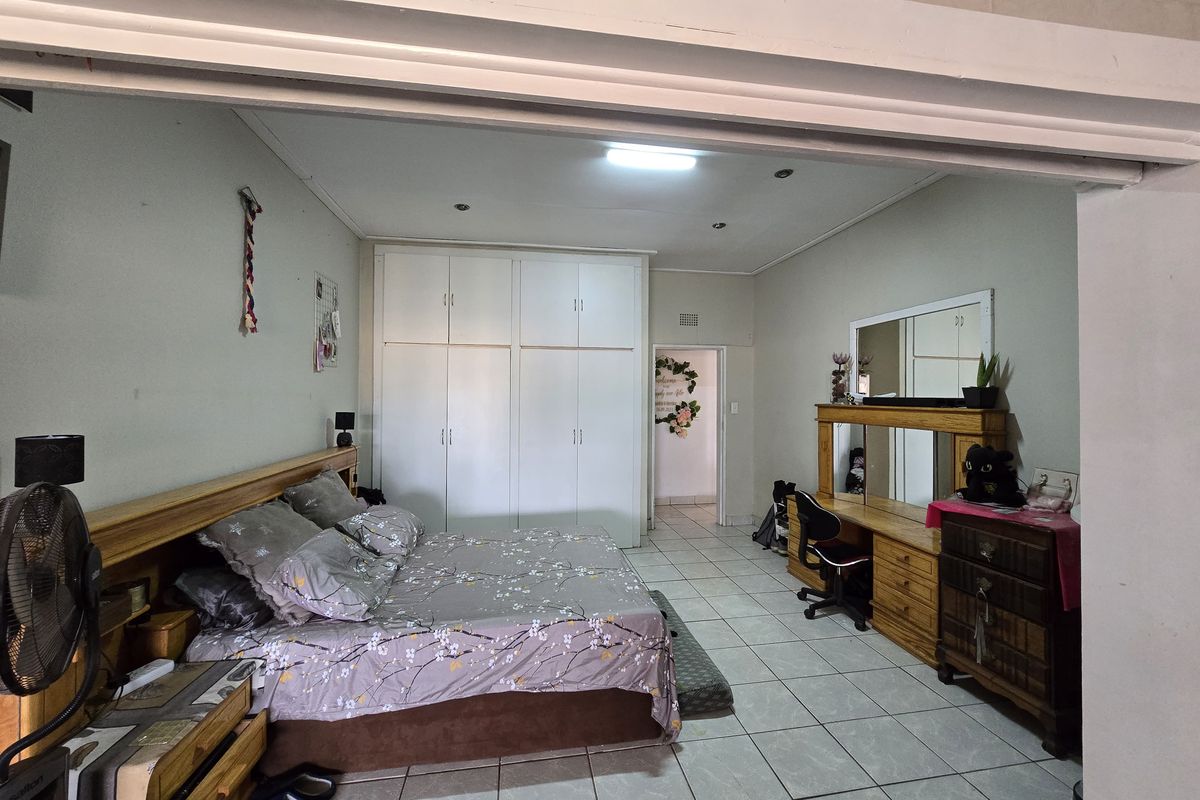 Spacious bedroom featuring built-in cupboards, tiled flooring, and recessed ceiling lighting, offering a functional layout with direct access to an adjoining room.