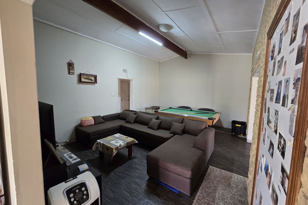 Spacious living area featuring a stone accent wall, exposed timber ceiling beam, and dark laminate flooring, currently utilized as a multi-purpose lounge and games room.
