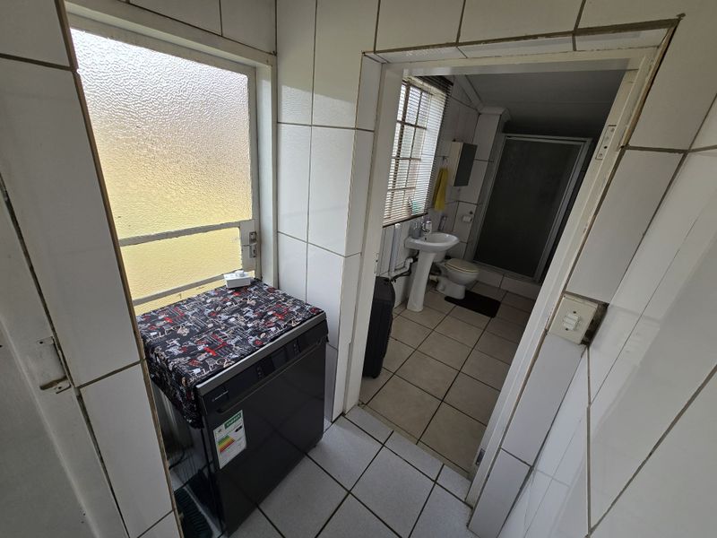 A functional laundry area featuring tiled finishes, leading into a bathroom equipped with a pedestal basin, toilet, and shower enclosure.