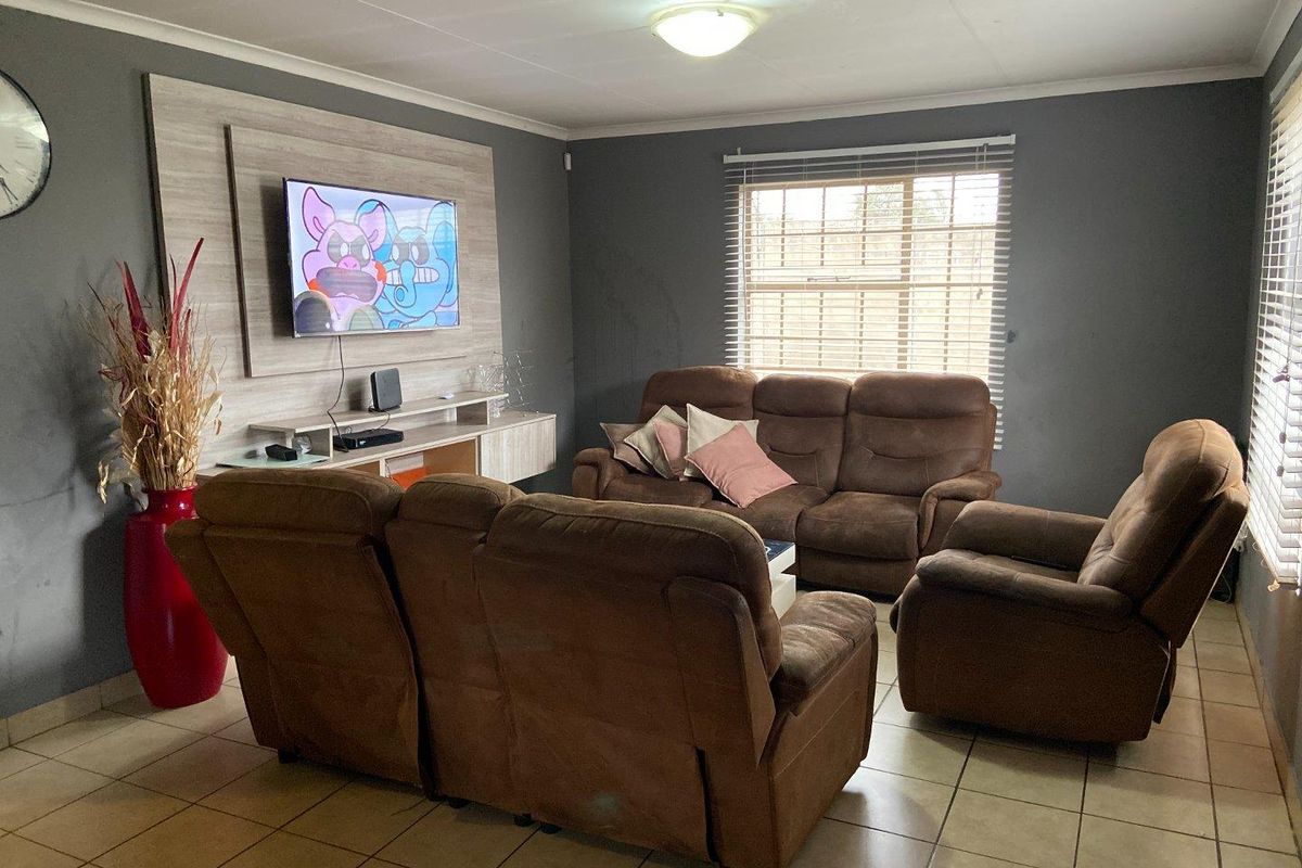 A living room featuring tiled flooring, a built-in media wall unit, and venetian blinds, providing a functional space for relaxation.