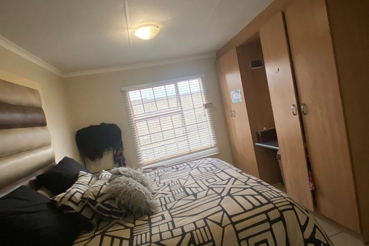A bedroom featuring built-in wooden cupboards, tiled flooring, and venetian blinds, providing a functional and neutral living space.