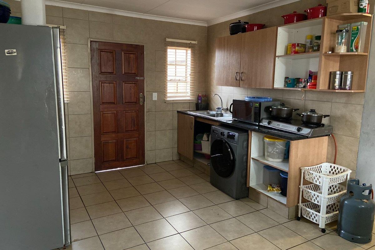 A functional kitchen featuring tiled walls and flooring, laminate cabinetry, and a built-in hob, offering a practical layout with direct exterior access.