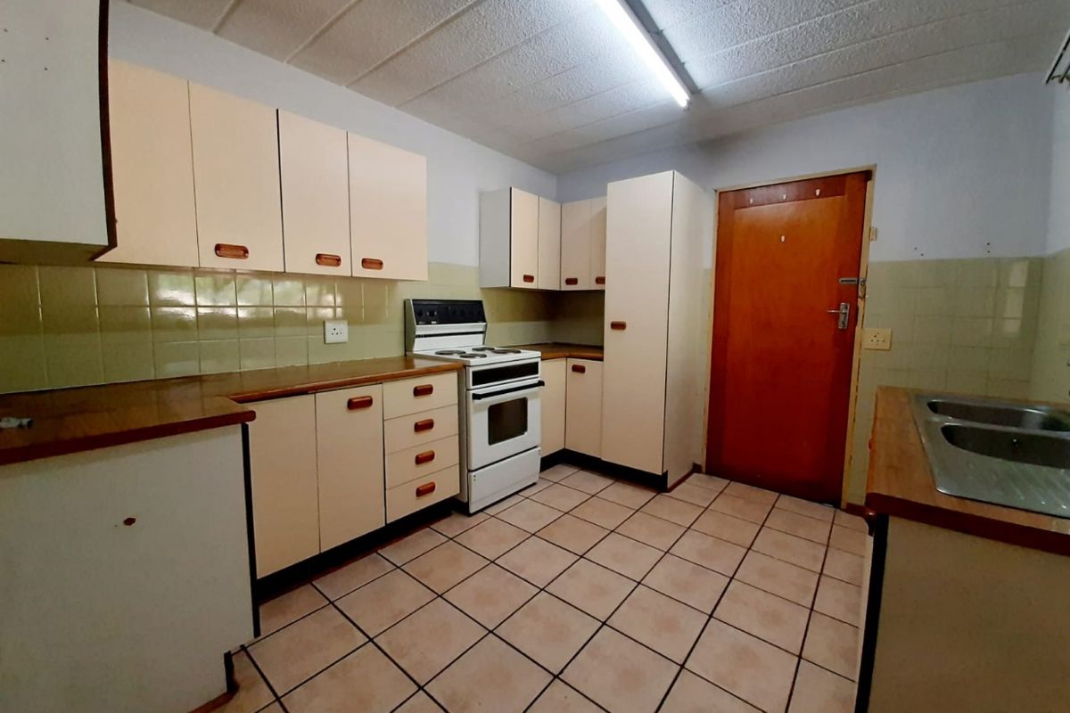 A dated kitchen featuring original cabinetry, tiled flooring, and a freestanding stove, offering a functional layout ready for modern renovation.