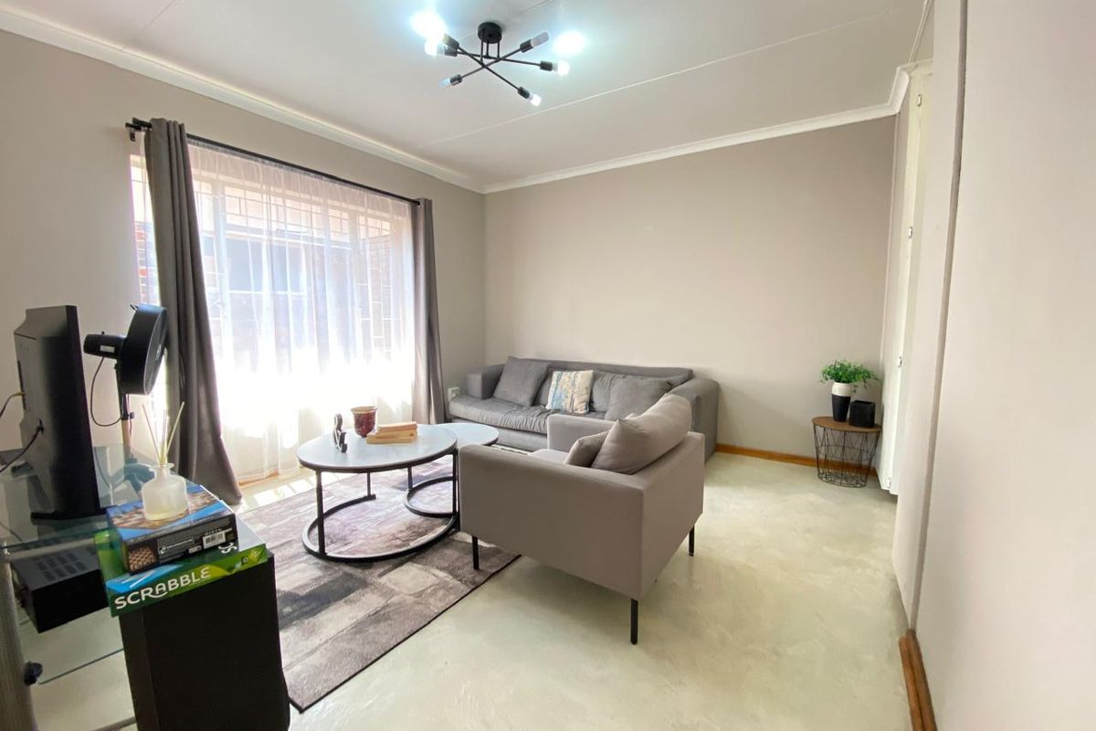 A bright and neutral living room featuring modern overhead lighting, large windows with curtains, and polished concrete flooring.