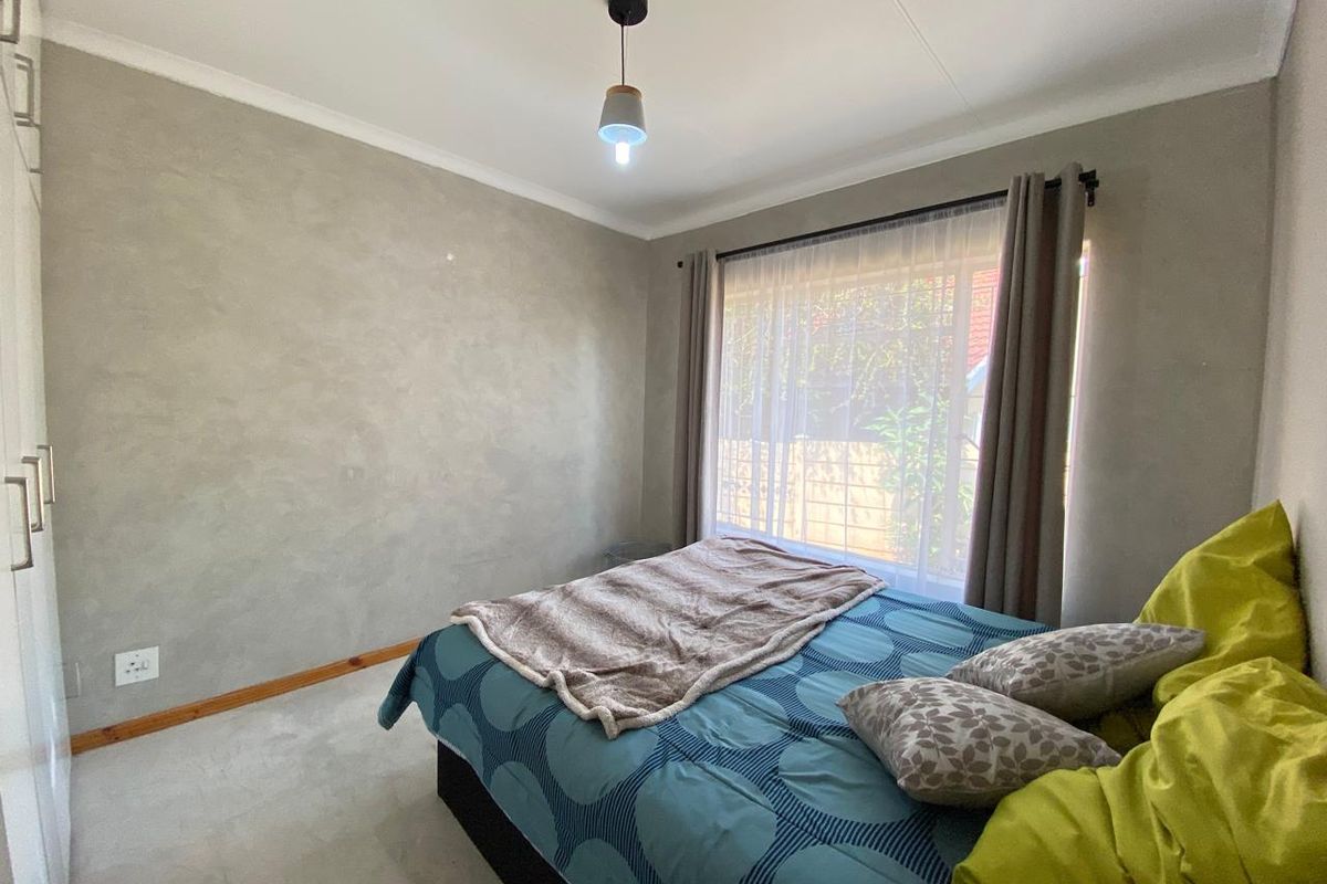 A bedroom featuring built-in cupboards, neutral textured walls, and a window with curtain tracks, providing a functional and well-lit sleeping space.