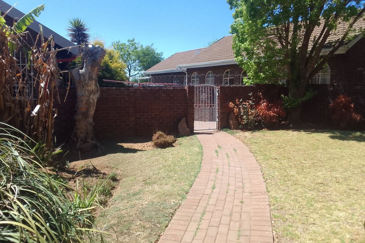 A rear garden area featuring a paved walkway leading to a metal pedestrian gate, enclosed by a brick boundary wall with security razor wire.