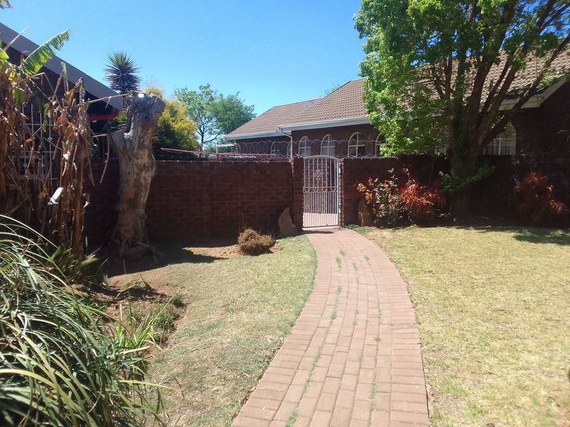 A rear garden area featuring a paved walkway leading to a metal pedestrian gate, enclosed by a brick boundary wall with security razor wire.