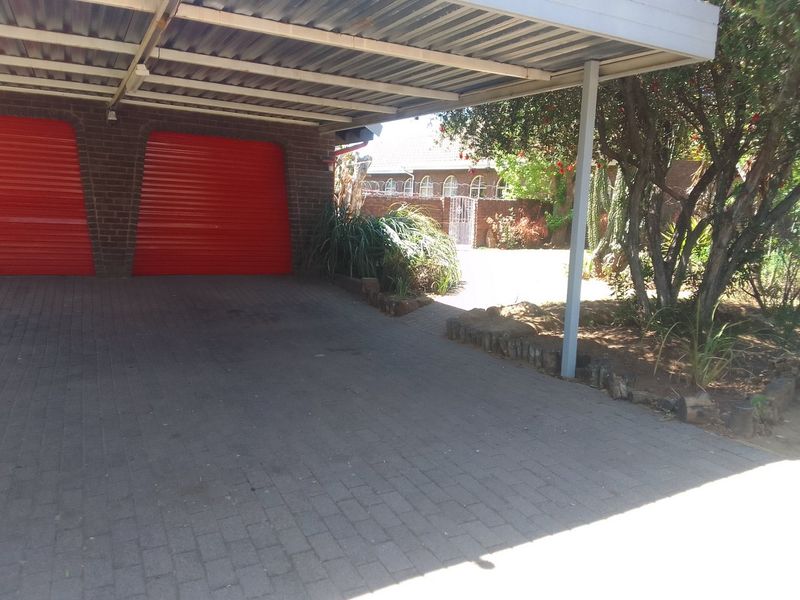 A covered carport area featuring double red roller garage doors and brick paving, providing secure off-street parking.