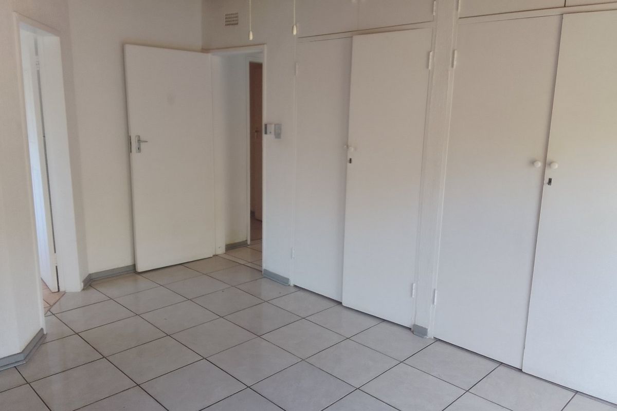 An empty bedroom featuring built-in cupboards, tiled flooring, and a timber ceiling, offering a blank canvas for renovation or interior design updates.
