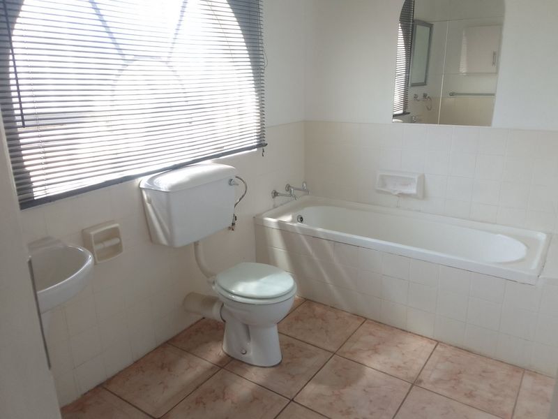 A functional bathroom featuring a built-in bathtub, wall-mounted basin, and toilet, finished with ceramic wall and floor tiles.