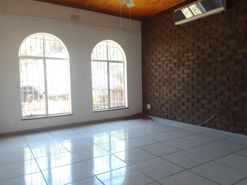 Spacious living area featuring an exposed brick feature wall, timber ceiling, arched windows with security bars, and polished ceramic floor tiles.